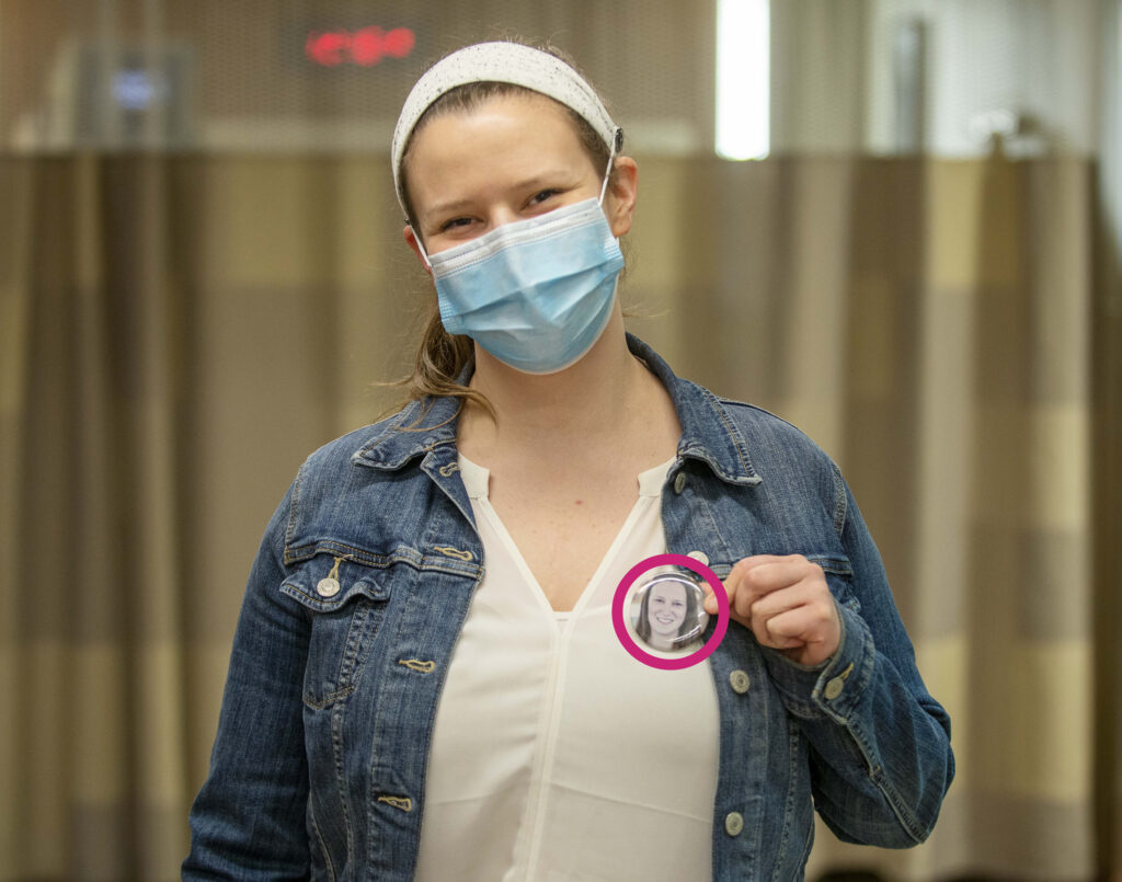 Emily wears a medical mask and also dons a button with her face so  people know what she looks like under the mask.