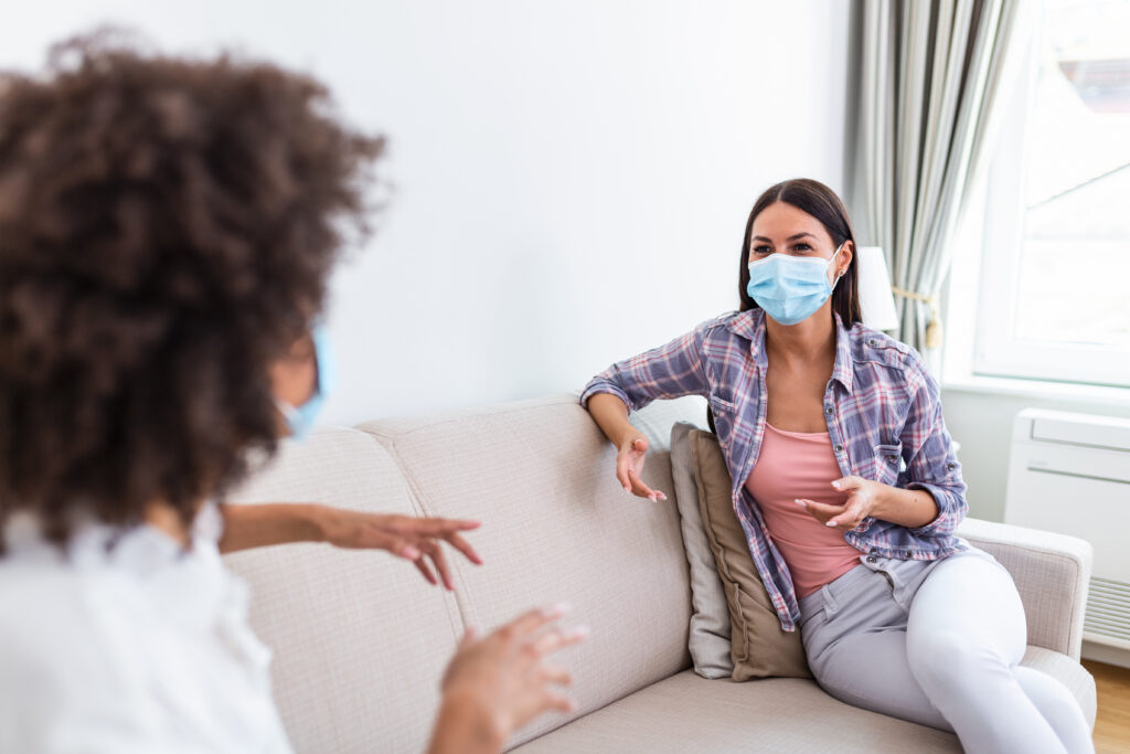 Two educators are seated, facing each other while they have a discussion. Each are wearing medical masks.