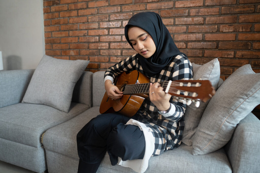 A person is seated on a couch and is playing the guitar.