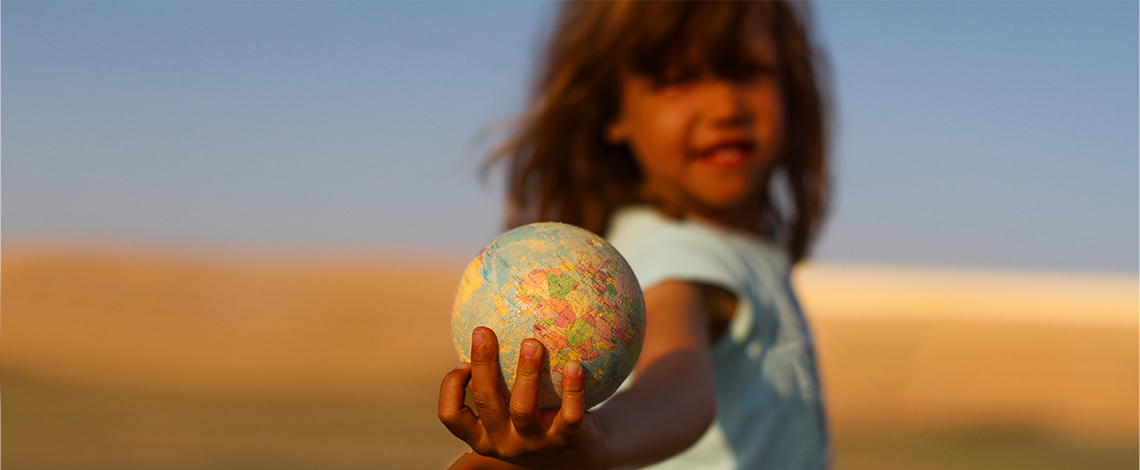 A child holds a globe in an outstretched hand