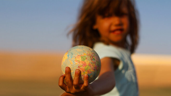 A small child holds a globe in their hand
