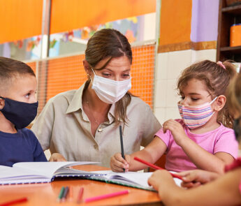 Educator and children with face masks in learning setting.