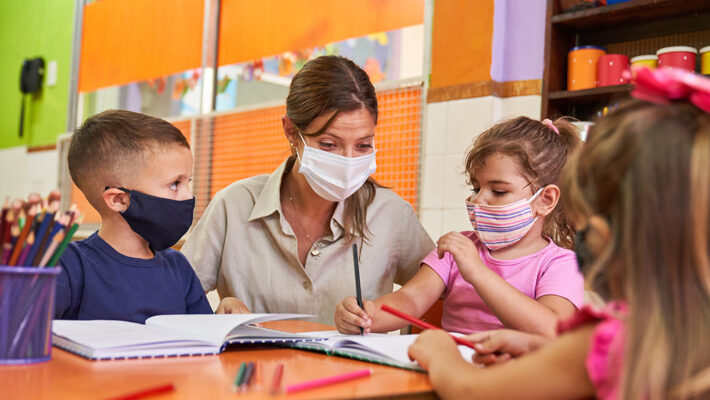 Educator and children with face masks in learning setting.