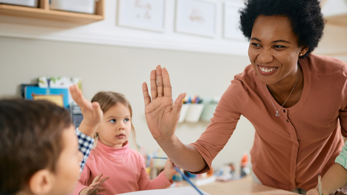 Image d’enfants à un bureau dans une classe faisant des activités. Une EPEI fait un high-five à l’un des enfants.
