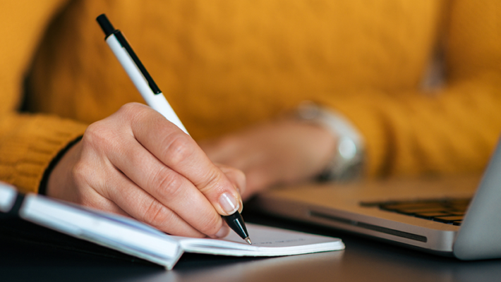 Image d’une personne prenant des notes sur un cahier avec son ordinateur devant elle.