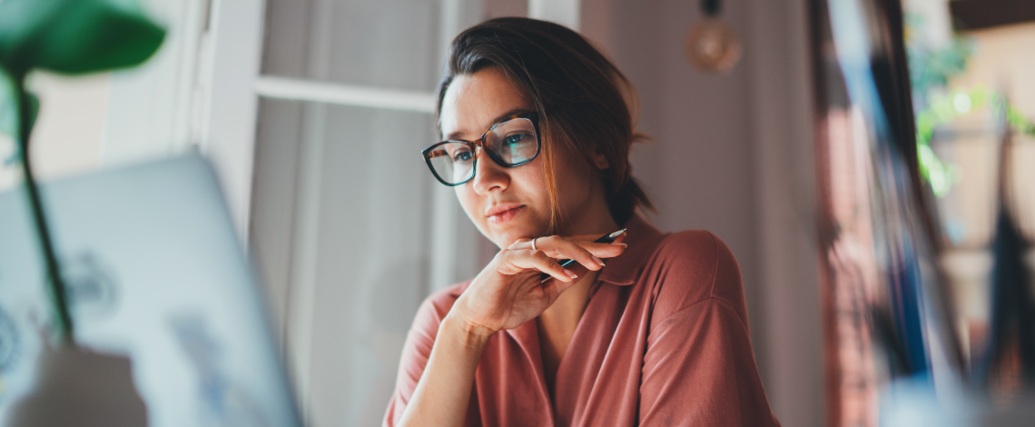 Femme qui regarde un écran d’ordinateur et réfléchit.